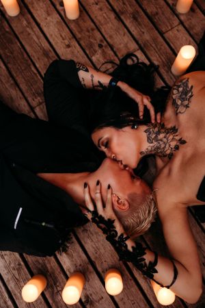 Romantic couple lying on wooden floor surrounded by glowing candles in moody lighting with black lace details.