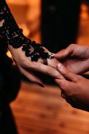 Close-up detail of hands preparing bride's delicate black lace sleeve with ring.