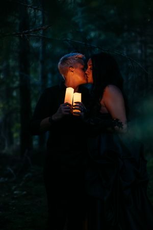 A romantic nighttime scene in a dark forest with a glowing candle illuminating two silhouettes sharing an intimate moment.