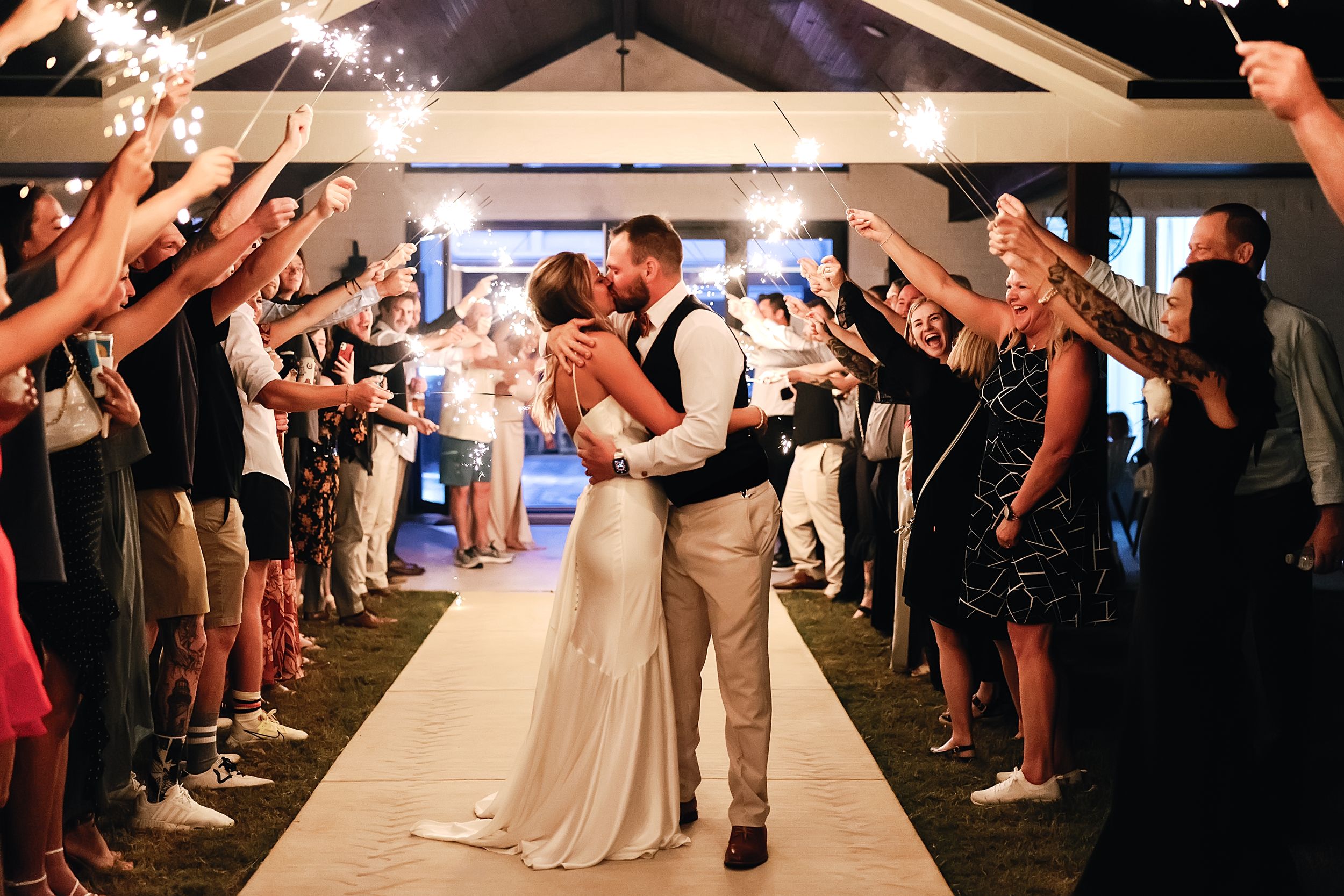 A wedding couple shares a tender moment while guests hold sparklers during their evening reception exit.
