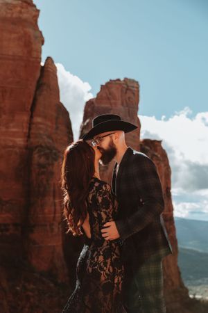 Romantic couple embraces against stunning red rock formations in desert landscape at sunset.