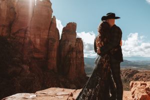 A silhouetted figure in a cowboy hat stands on red rock formations overlooking a vast desert landscape.