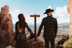 A couple in western attire holding hands while looking out at scenic red rock formations in the desert landscape.