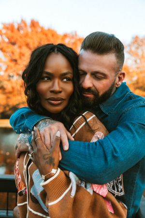 A romantic autumn portrait of a couple embracing outdoors with vibrant orange fall foliage in the background.