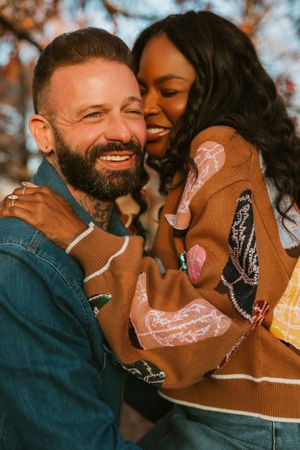 An intimate portrait of a couple laughing and embracing while wearing casual denim and brown clothing outdoors.