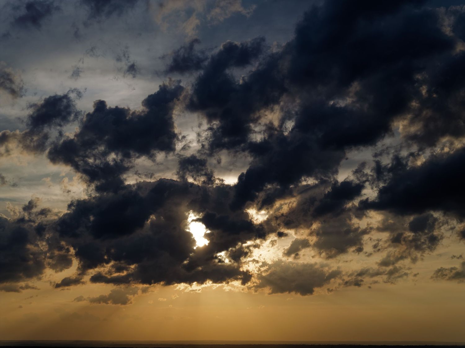 Dark storm clouds silhouette against a golden sunset sky creating a dramatic panoramic view.