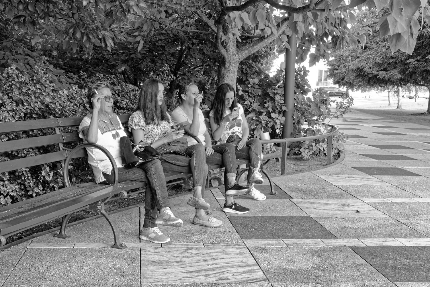Street photography of likeness of lady's body language relaxing on park benches under shade trees on sunny afternoon.