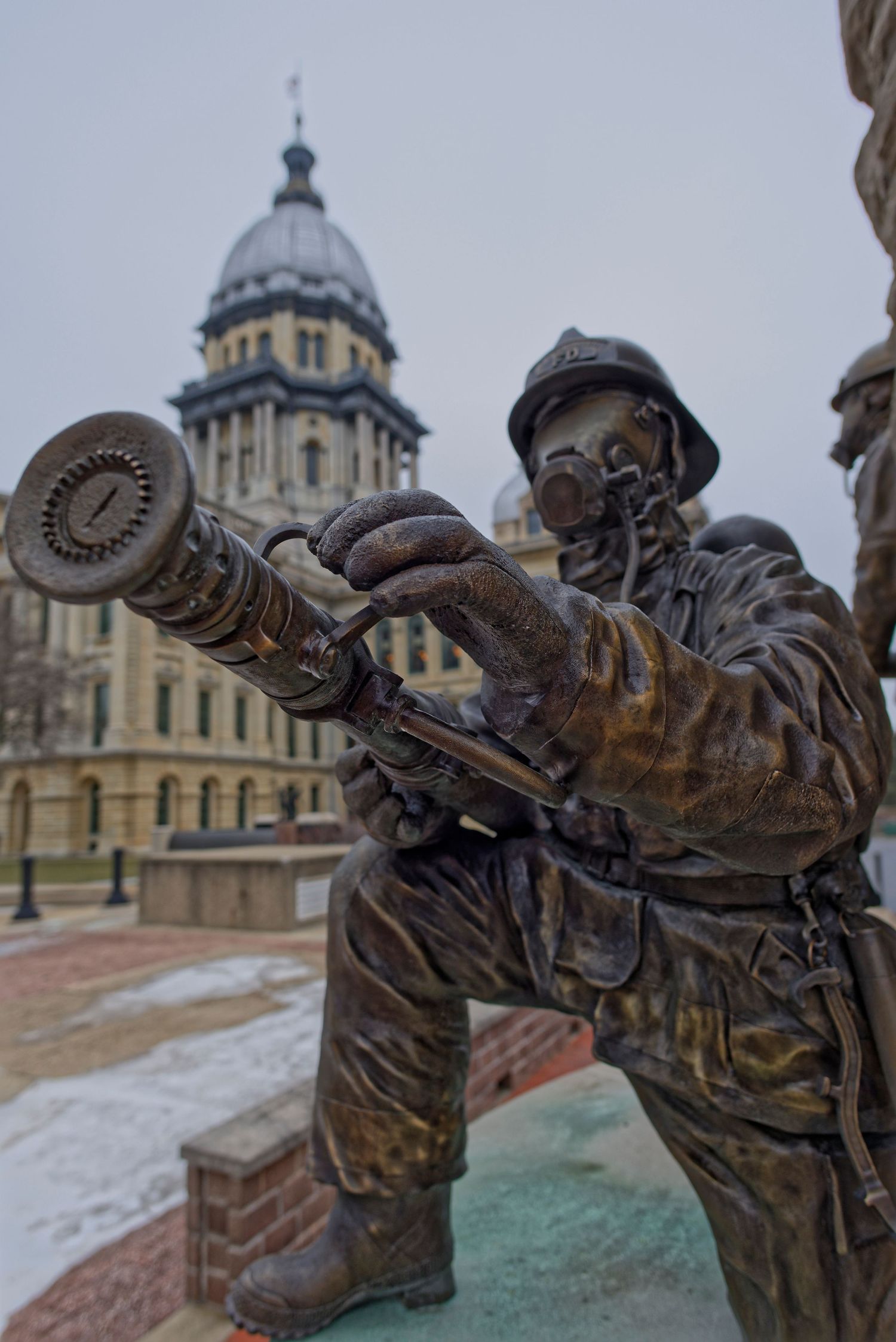 Bronze firefighter statue holding a hose stands in front of Illinois State Capitol building dome in Springfield.
