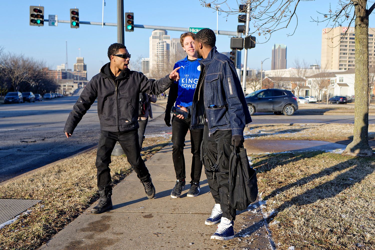 Three people in athletic wear stand on a sidewalk during a sunny winter day with a city skyline in the background.