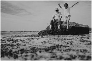 Two people standing triumphantly on a rocky outcrop overlooking the ocean.