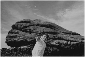 Black and white portrait with dramatic rock formation looming in the background.