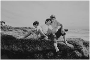 Three people relaxing on large coastal rocks overlooking the ocean.