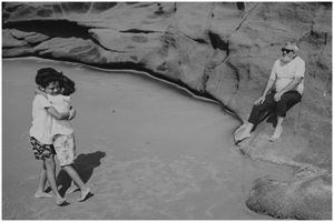 People enjoying a sunny day by a tidal pool among coastal rock formations.