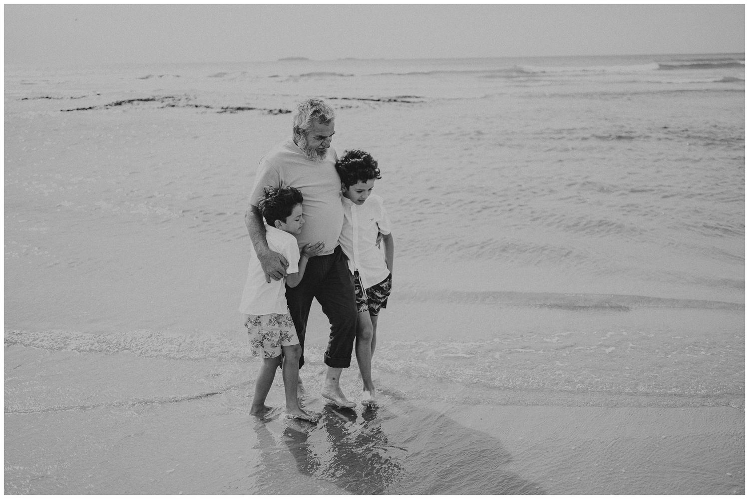 Three people standing in shallow ocean water together in a black and white photo.