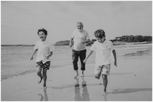 Three people running joyfully along the water's edge on a beach.