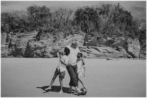 Two people playfully walking together on a sandy beach with rocky cliffs in the background.