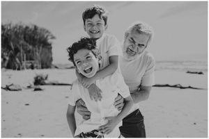 Three people embracing and laughing together on a sunny beach.