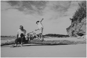 People playing and jumping on a beach with dramatic cliffs and cloudy sky in the background.