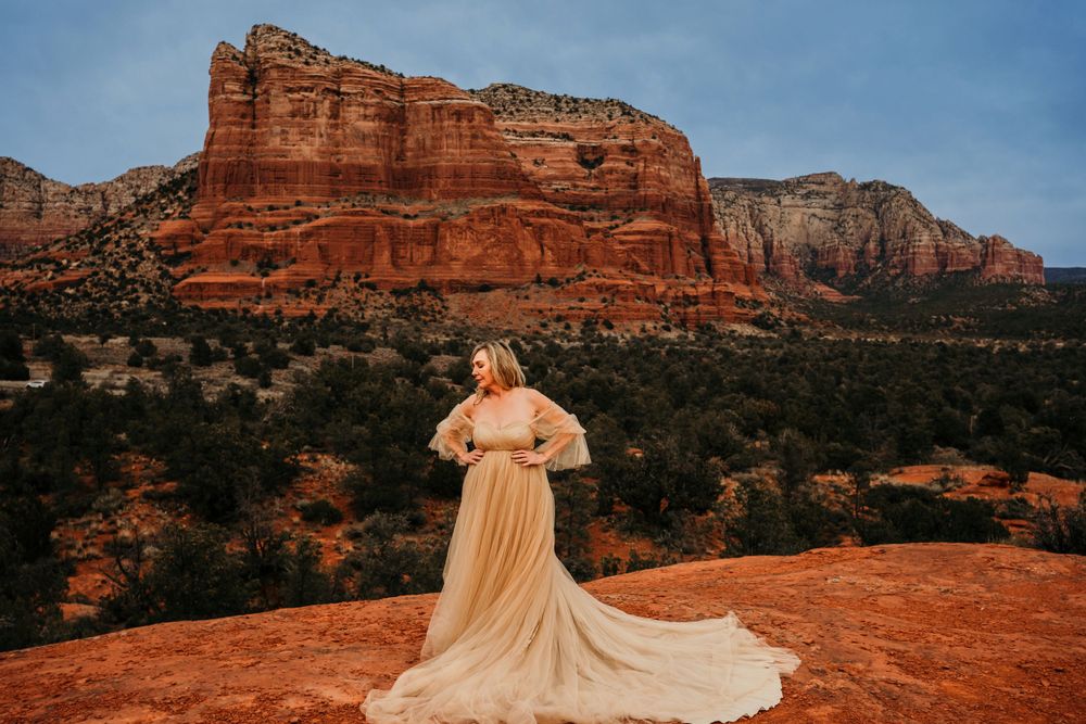 A flowing cream dress contrasts against red rock formations in Sedona's desert landscape at sunset.