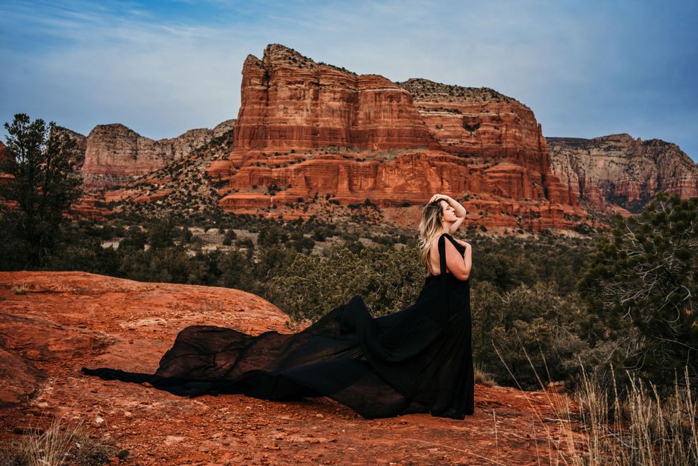 Long black dress creates striking contrast against towering red sandstone cliffs in Sedona.