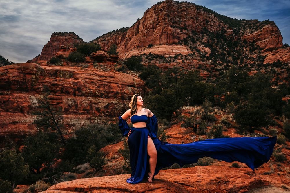 Royal blue dress flows dramatically against red rock formations in Sedona's landscape.