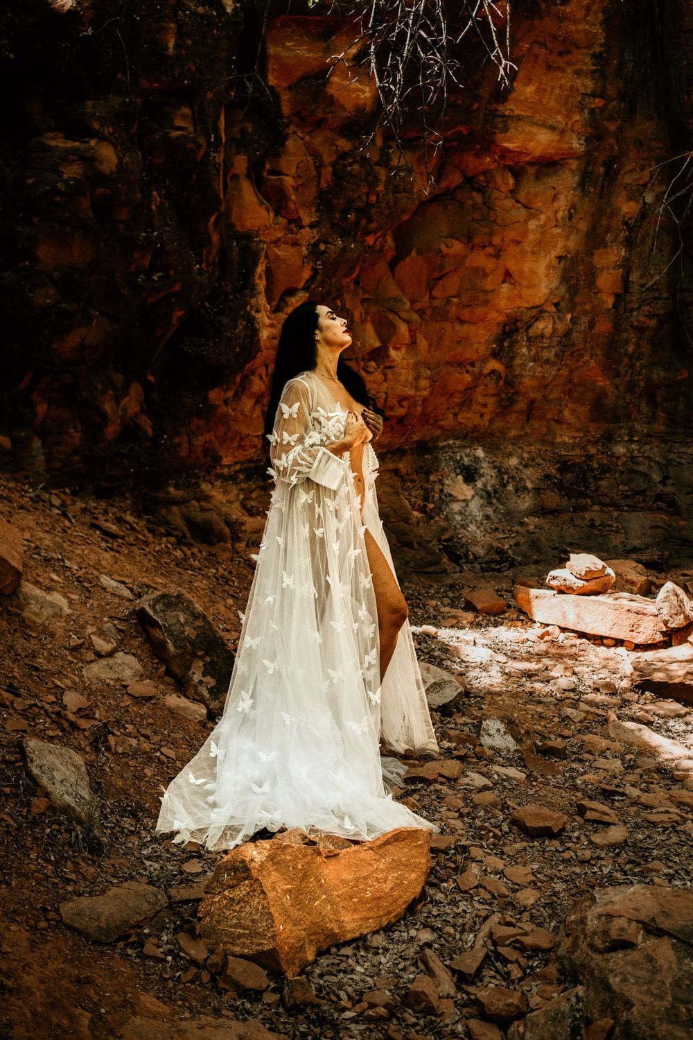 Delicate lace white dress creates ethereal scene against rustic cave walls.