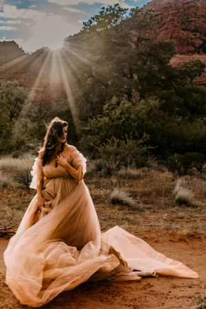 Ethereal peachy gown flows in desert sunburst among red rock formations.