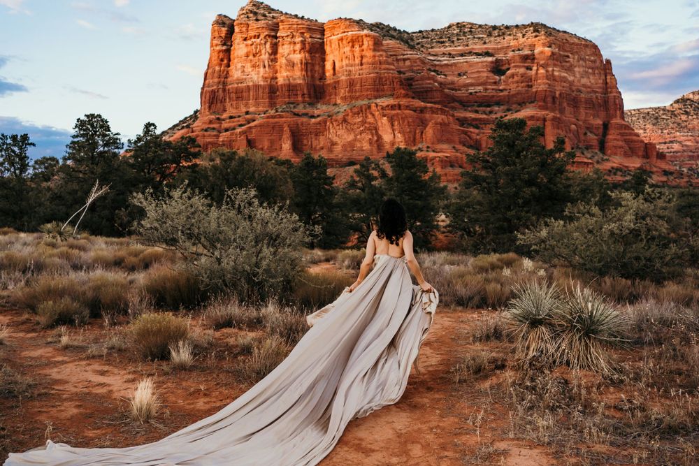 Long flowing white train extends across red desert landscape with towering rock formation.