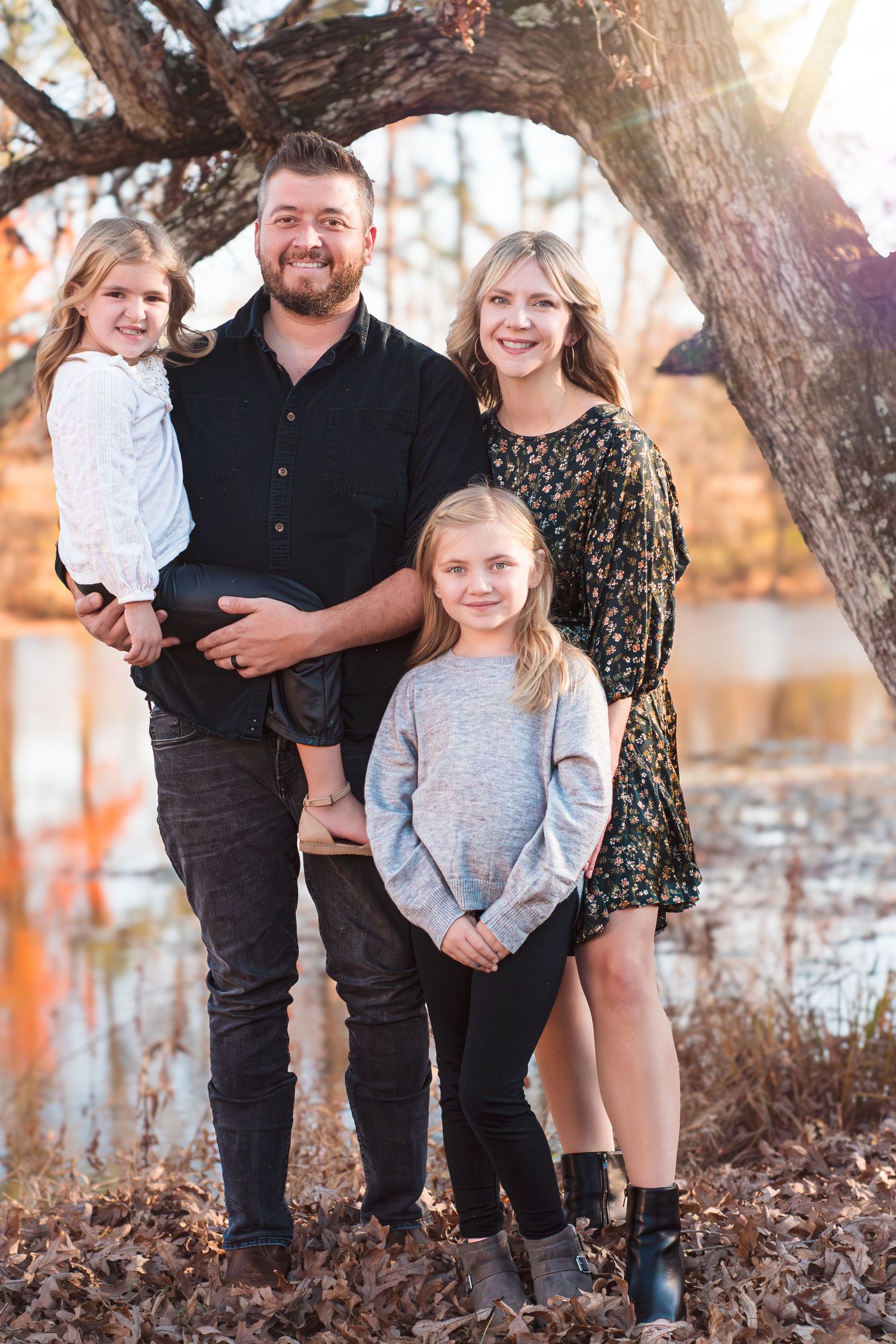 Family of four posing together under a tree during golden hour in autumn.