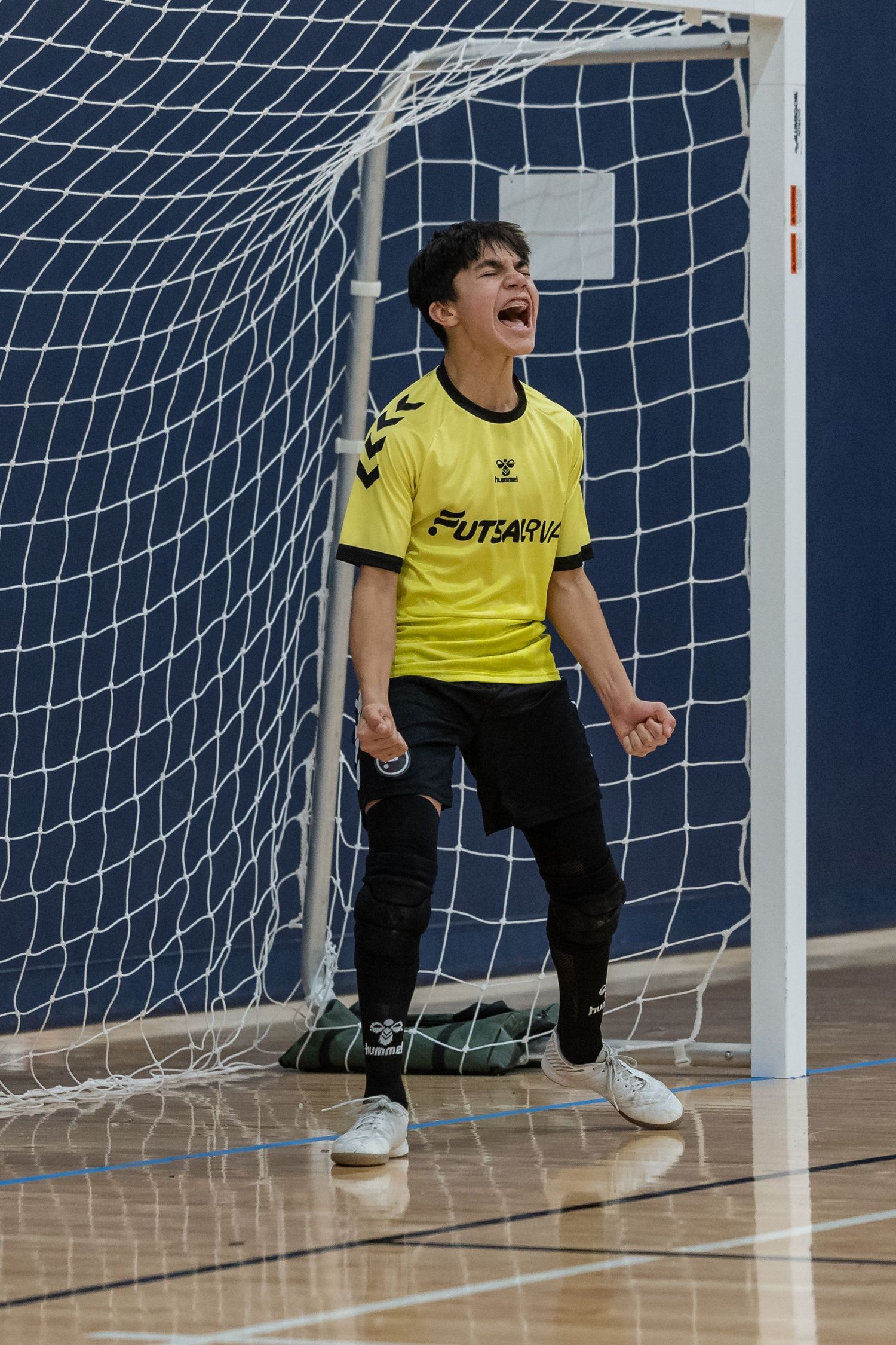 Goalkeeper in yellow uniform crouching in front of soccer goal net during practice.