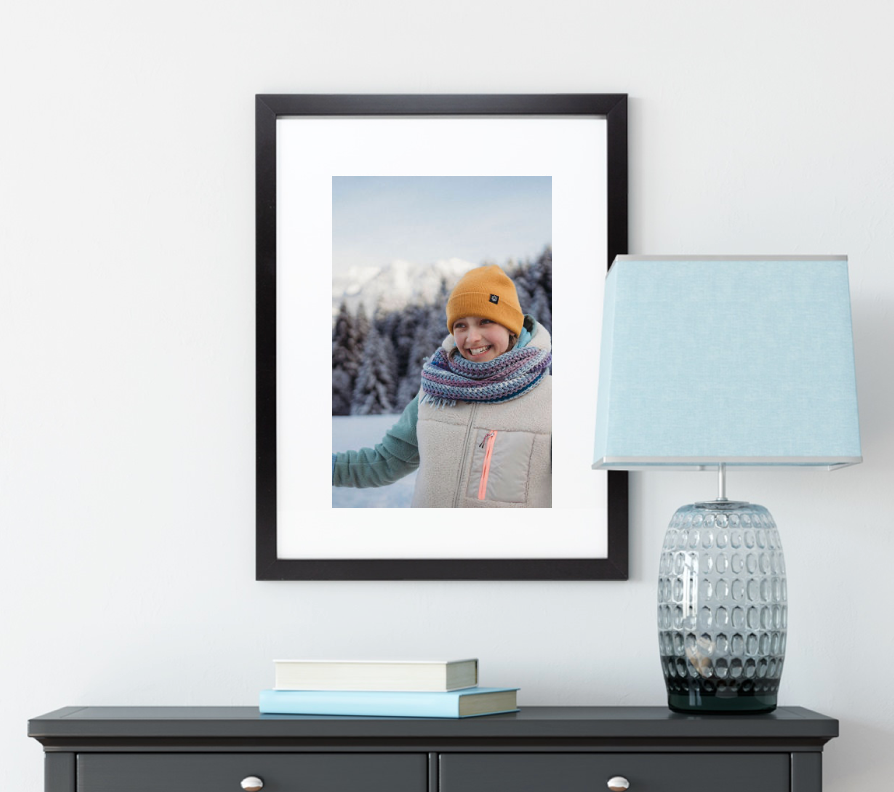 Black framed winter photo displayed above console table with blue lamp and textured glass base in modern room decor setting.