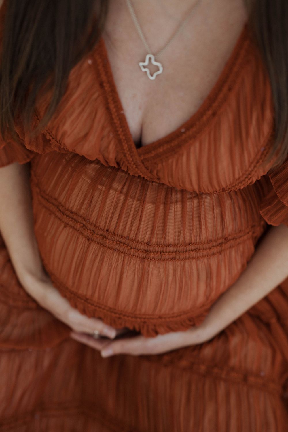 Close-up of someone wearing a rust-colored pleated dress with delicate ruffle details and a small pendant necklace.