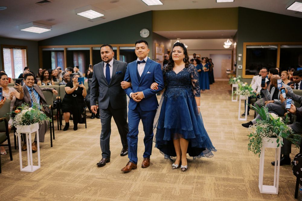 Wedding processional walking down aisle in venue decorated with lanterns and greenery.