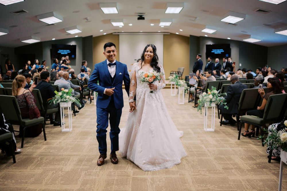 Wedding ceremony processional in an indoor venue with floral aisle decorations.