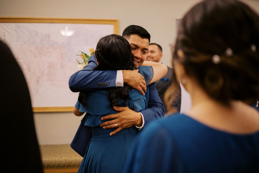 Wedding party members share emotional embraces in a room during a special moment.