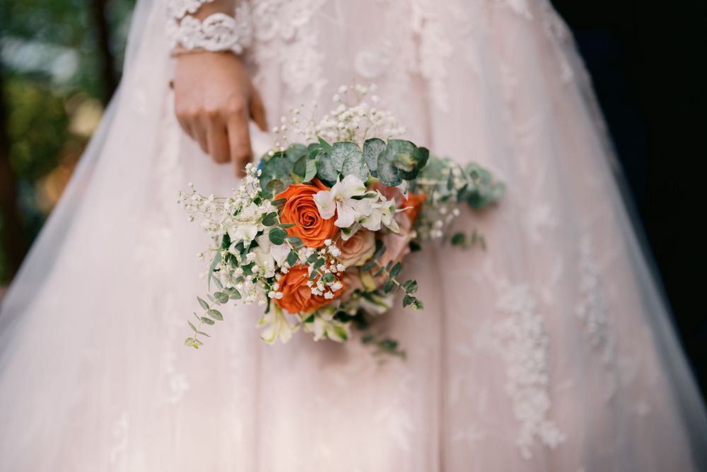 Close-up of a stunning bridal bouquet with orange roses and eucalyptus against a pink lace wedding dress.