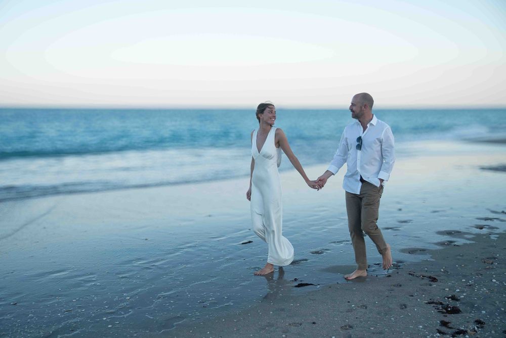 Kari and Jeff taking a stroll while looking at each other and holding hands on beach on Worth Ave