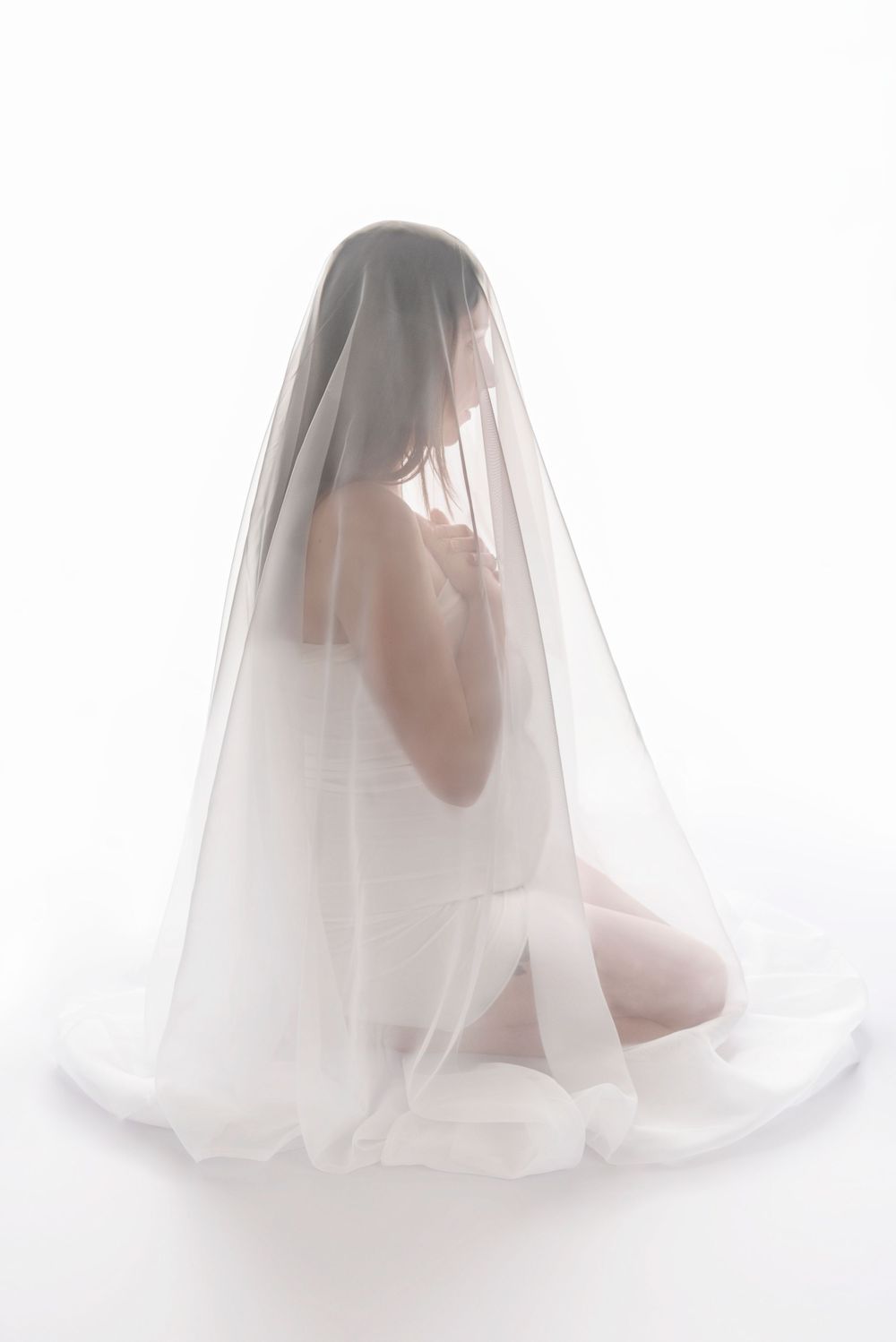 Ethereal artistic portrait of a figure draped in a sheer white veil against a bright white background.