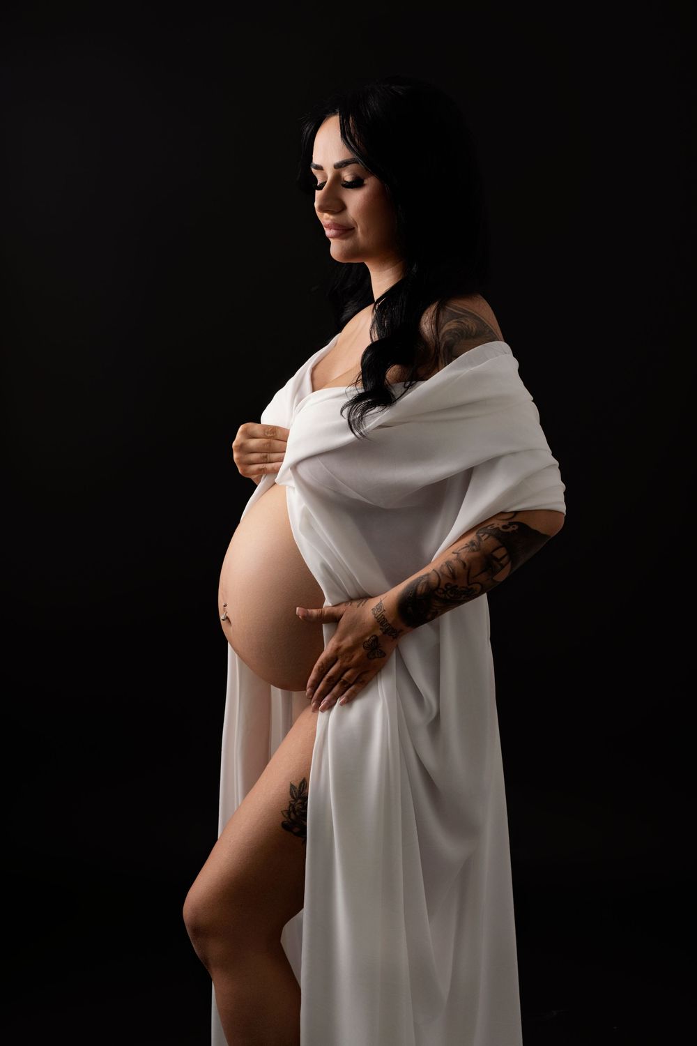 Artistic maternity photo with woman in white fabric against dark background.