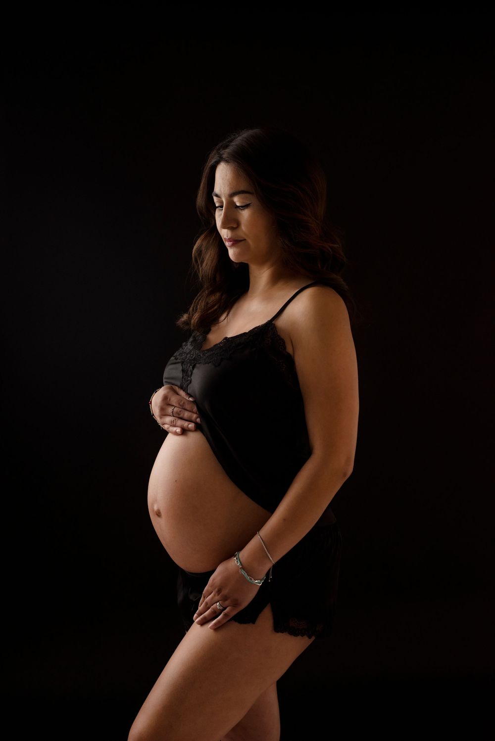 Artistic maternity photos in black showing silhouette and belly against dark background.