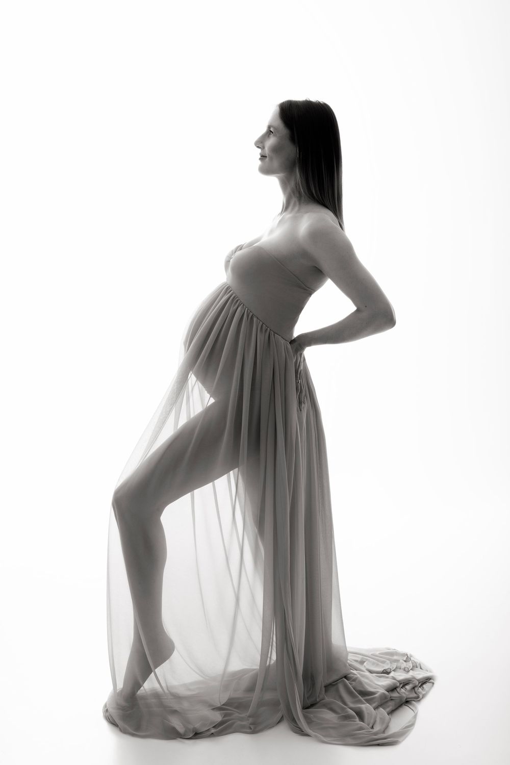 Artistic black and white maternity photo showing silhouettes of a pregnant woman in flowing white fabric.