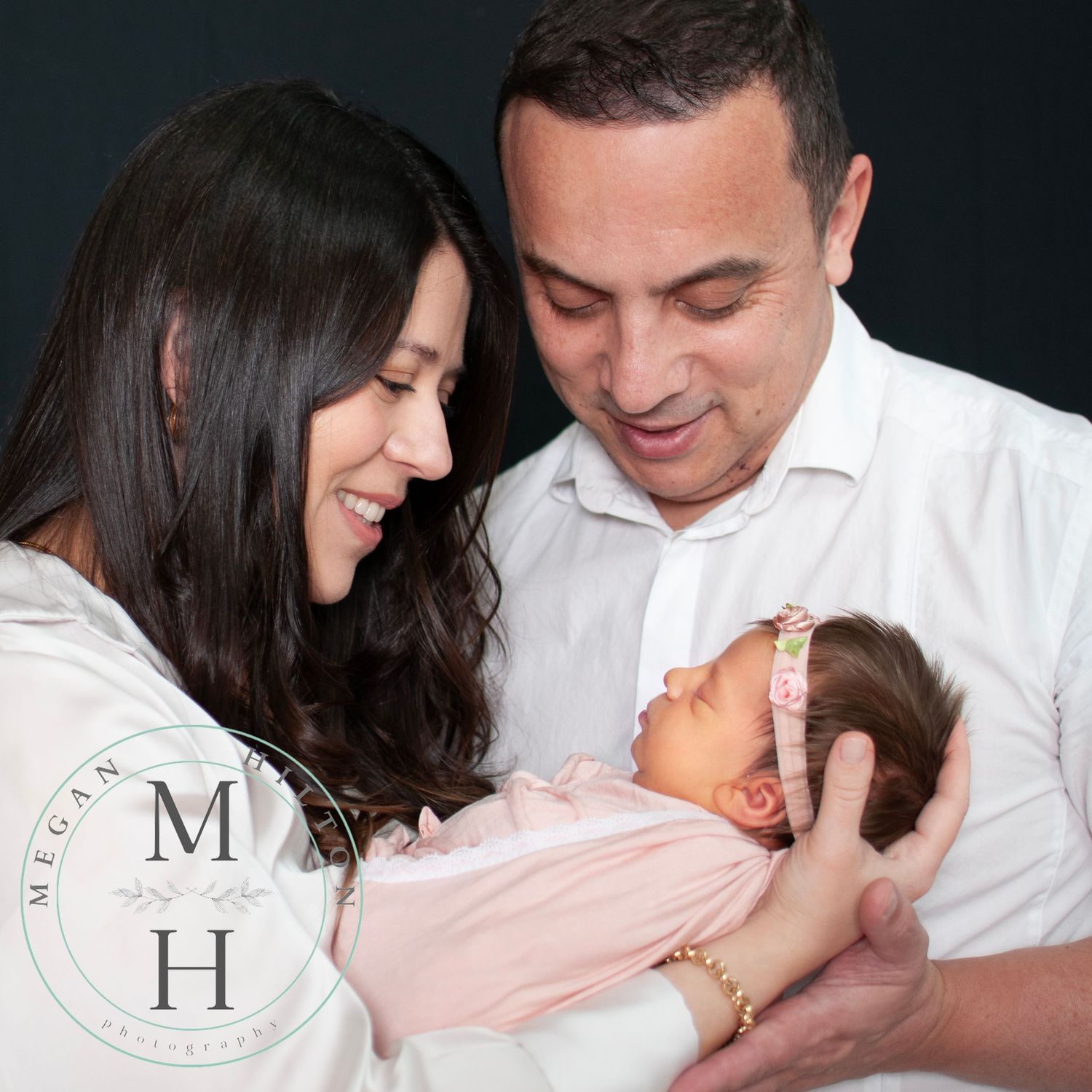 Parents holding newborn against black backdrop, close up