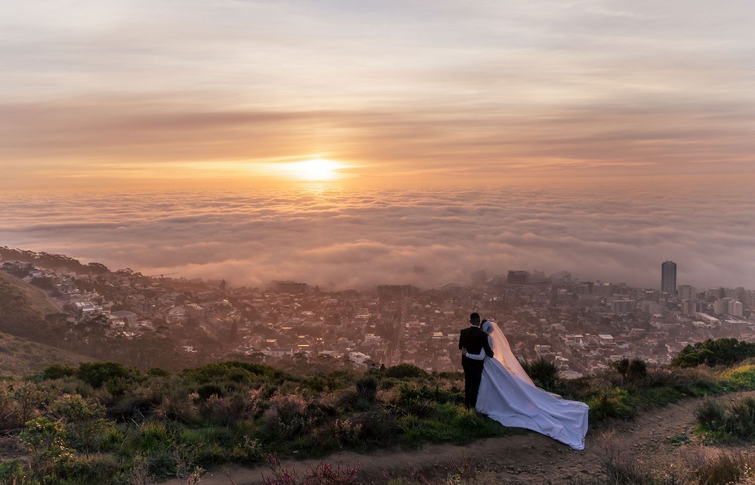 Silhouettes against a dramatic sunset skyline showing sweeping views from a mountain vantage point.