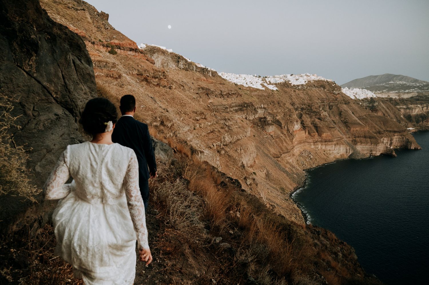 A photo of a bride and groom at their elopement against the caldera cliffs of Santorini, Greece