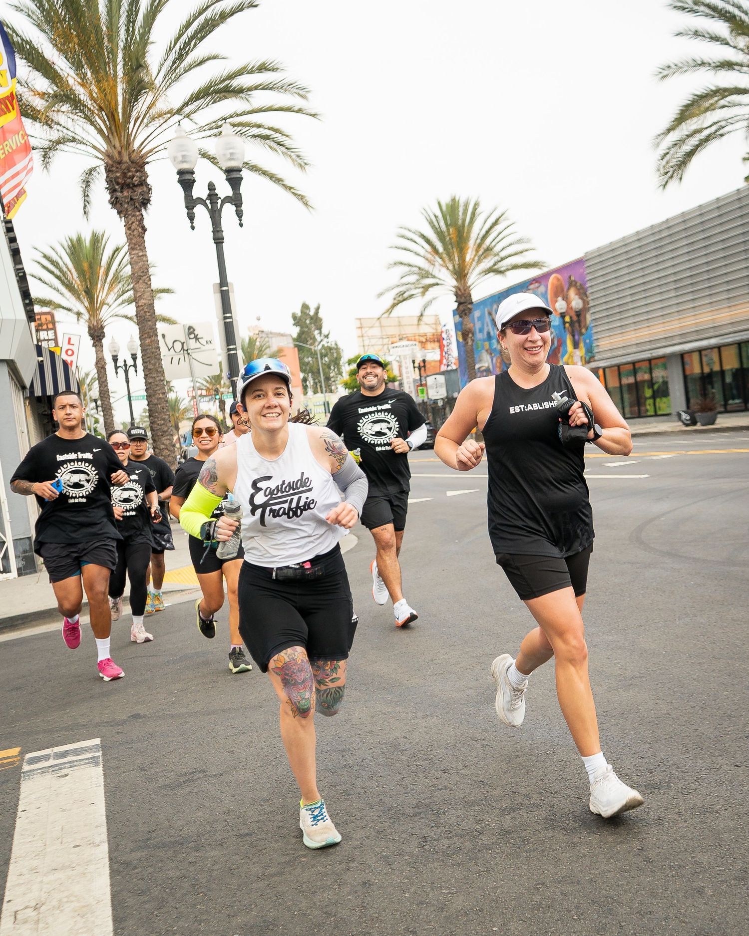 Group of runners in athletic gear jogging down a palm-lined city street during a race.