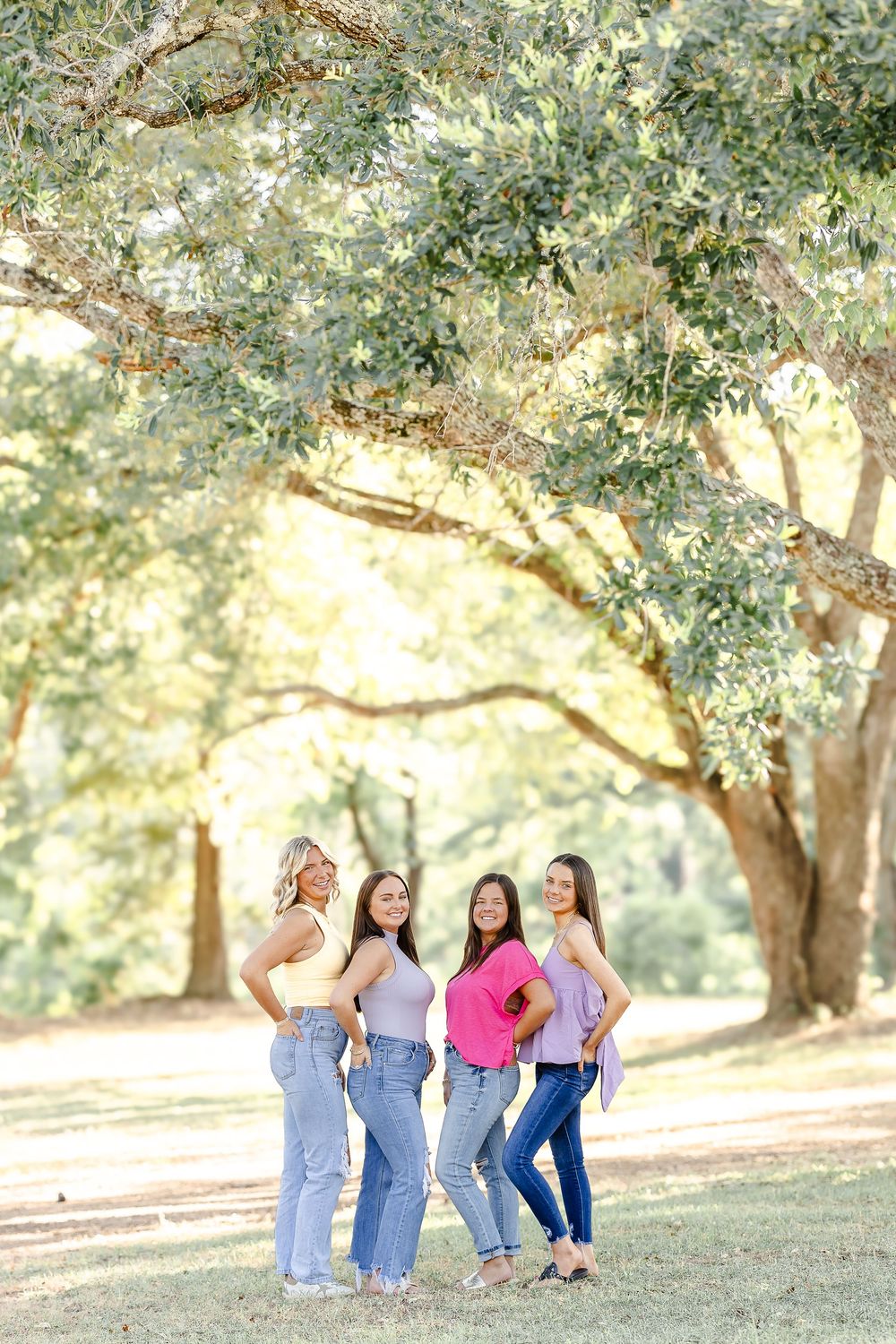 A group stands together under a large oak tree in a sunlit park setting on a warm afternoon.