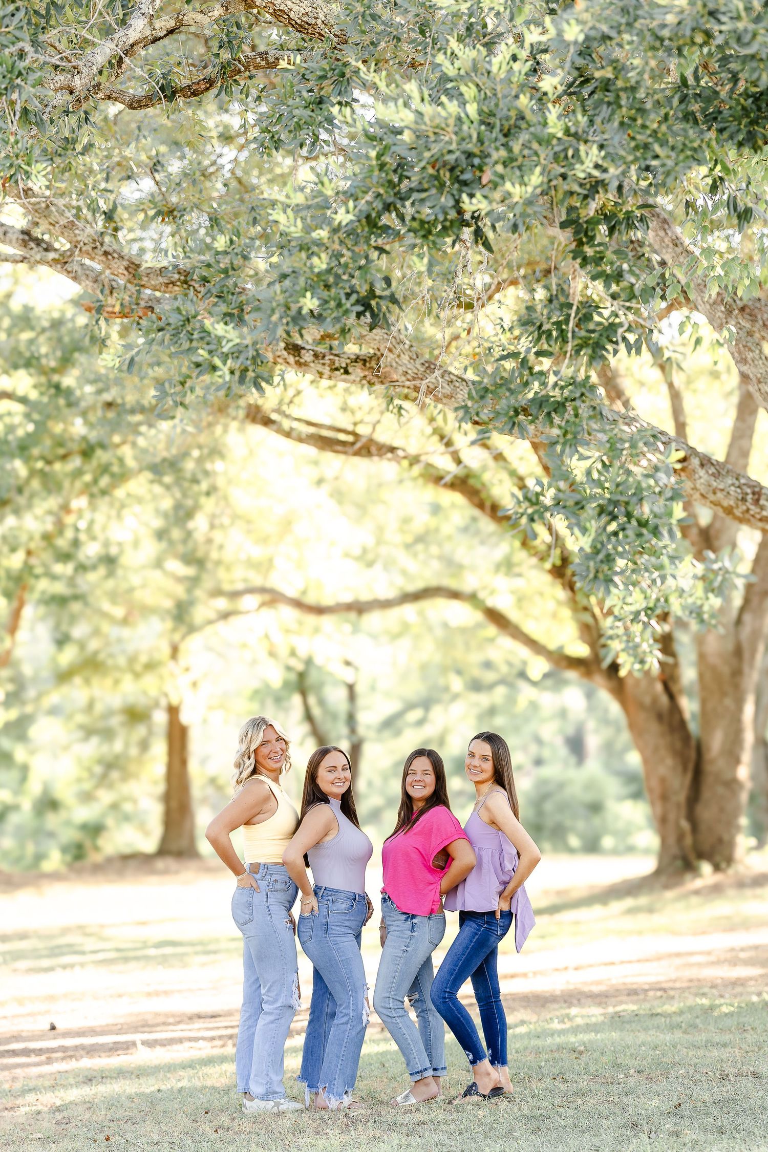 A group stands together under a large oak tree in a sunlit park setting on a warm afternoon.