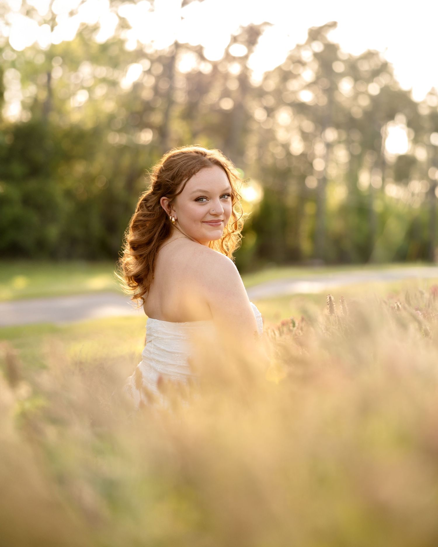 Golden sunlight illuminates a dreamy outdoor portrait in a field as warm evening light filters through tall grass.