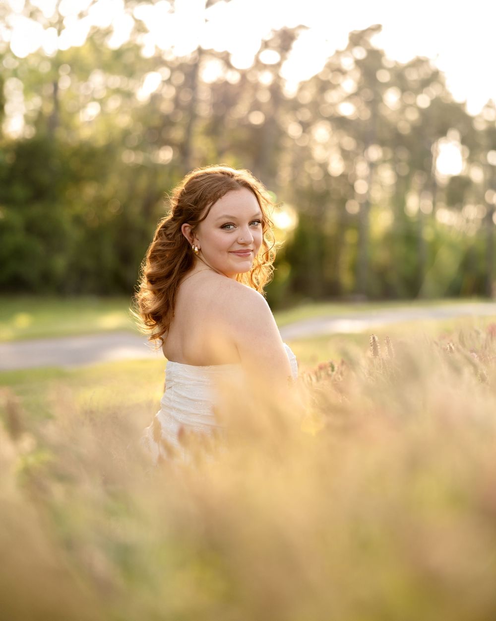 Golden sunlight illuminates a dreamy outdoor portrait in a field as warm evening light filters through tall grass.