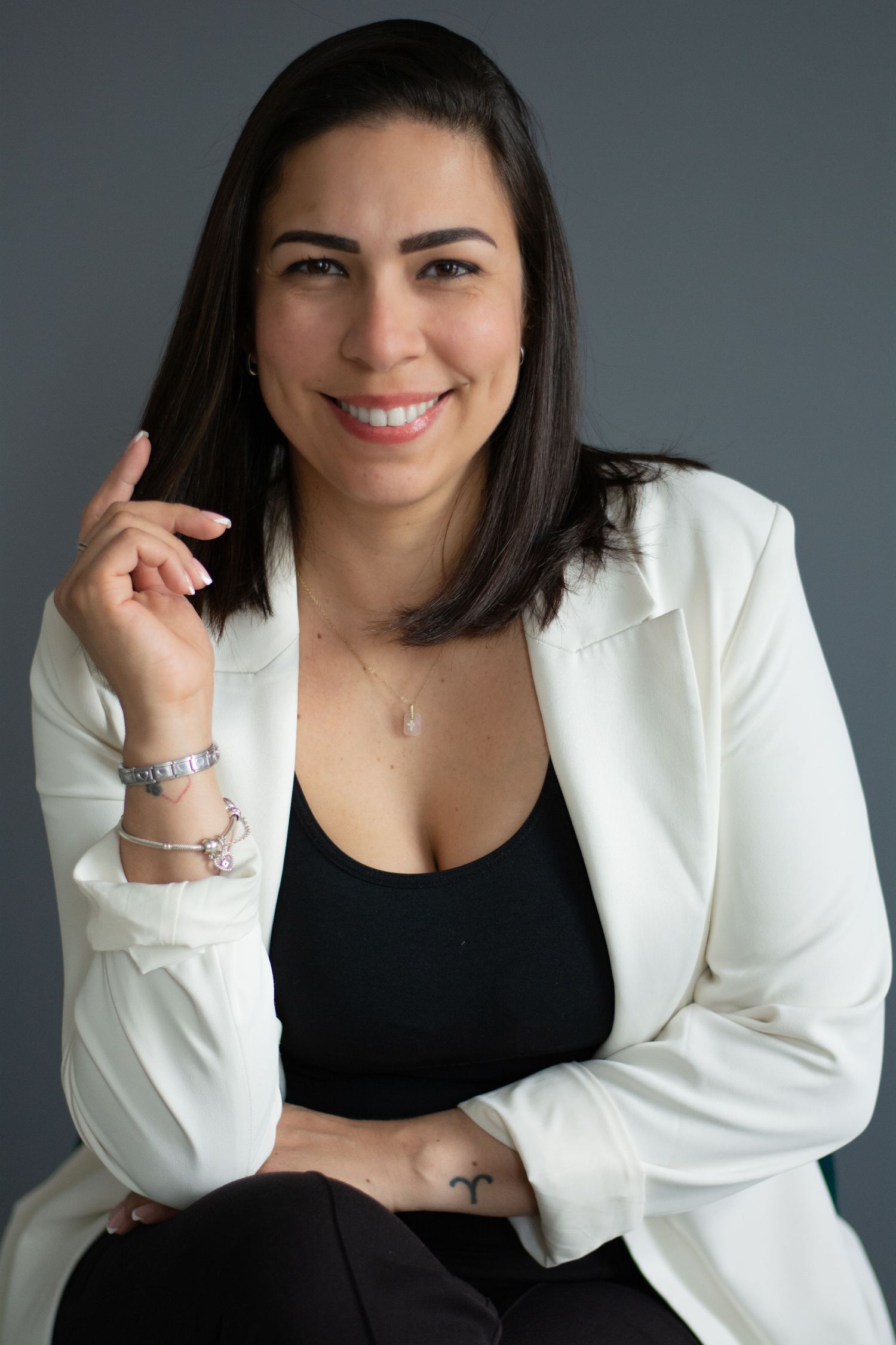 Professional wearing a white blazer and black top poses confidently against a gray background.